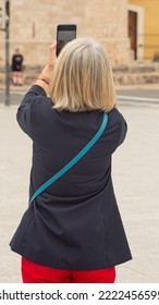 Older Woman From The Back With Blonde Hair Taking A Picture With Her Personal Mobile