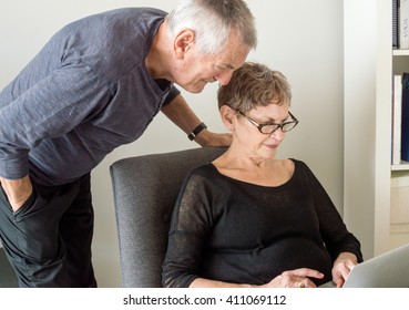 Older Woman In Black Clothing Seated Using A Computer With Older Man In Dark Clothing Looking Over Her Shoulder