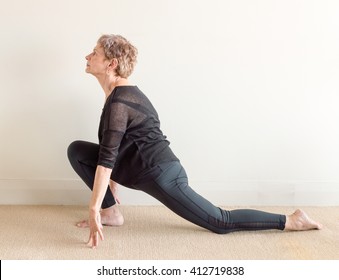 Older Woman In Black Yoga Clothing In Lunge Yoga Posture On Floor