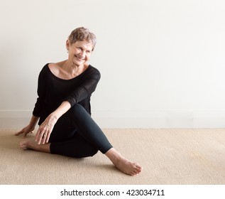 Older Woman In Black Yoga Clothing Laughing In Relaxed Seated Yoga Posture