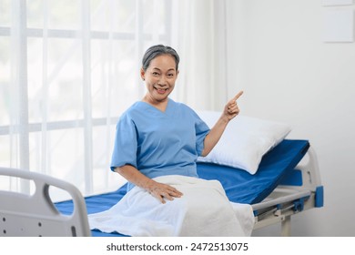 Older woman in a blue hospital gown is pointing to something. She is smiling and she is happy - Powered by Shutterstock