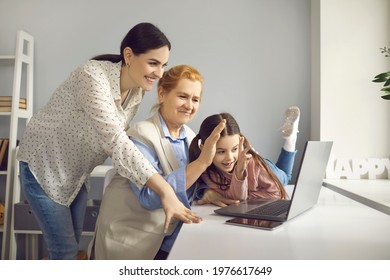 Older Woman With Daughter And Little Granddaughter Waving Her Hand During A Video Call. Women Communicate With Family Online Using Laptop. Concept Of Modern Technology And Different Generations.