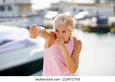 Older woman doing sport in a coastal port. Arm training throwing boxing punches. Mature Female doing shadow boxing outdoors. - Powered by Shutterstock