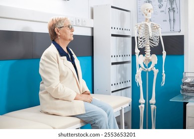 Older woman dressed casually sits in a hospital room prepared for her health consultation. Senior caucasian lady waits on examination bed for medical checkup in doctors office. - Powered by Shutterstock