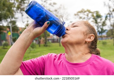 Older Woman Drinking Water After Exercising In The Park