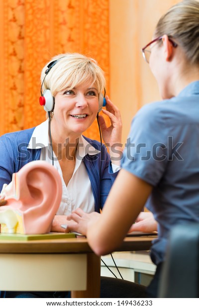 Older woman or female pensioner with a hearing\
problem make a hearing test and may need a hearing aid, in the\
foreground is a model of a human\
ear