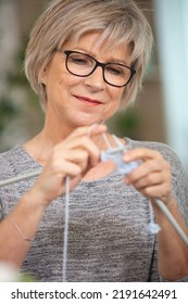 Older Woman In Glasses Sitting And Sewing