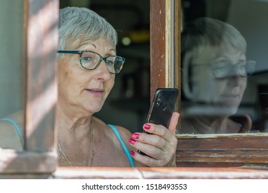 Older Woman With Glasses Talking With Mobile Phone Looking Out The Window