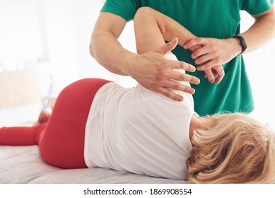 Older Woman Have A Visit In Clinic, Lying Down And Having Rehabilitation. Male Instructor Helping Her.