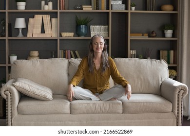 Older Woman In Headphones Visualize While Listen Audio Affirmations Records Feels Serenity Seated Cross-legged On Sofa At Home. Hobby, Calmness, Improve Self-awareness Through Meditation Music Concept