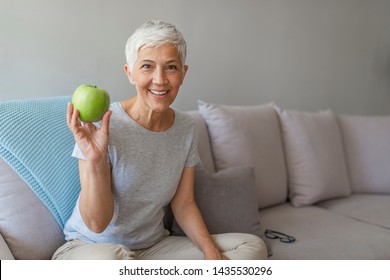 Older Woman With Healthy Food Indoors. Happy Senior Woman With Green Apple At Home. Senior Woman Holding An Apple. Age, Healthy Eating, Food, Diet And People Concept