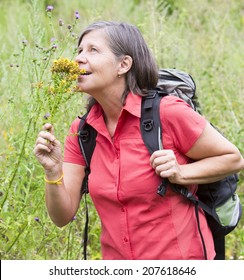 Older Woman Is Hiking In Nature And Smelling Flowers