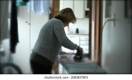 Older Woman Ironing Clothes, Candid Domestic Housewife At Laundry Room