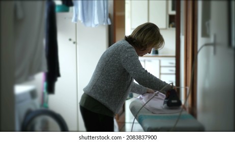 Older Woman Ironing Clothes, Candid Domestic Housewife At Laundry Room