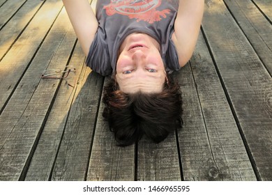 Older Woman Laying On Wooden Floor Upside Down. Take Off Glasses And See On Sunny Day.