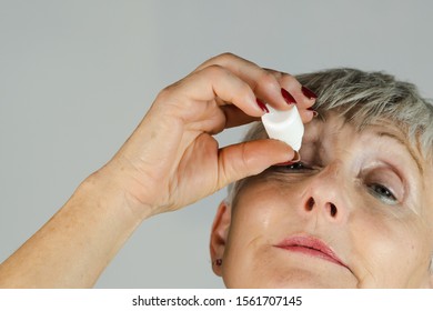 Older Woman Looking Up Applying Eye Drops On White Background