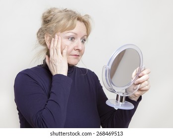 An Older Woman Looking In A Hand Mirror On Her Face