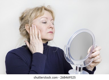 An Older Woman Looking In A Hand Mirror On Her Face