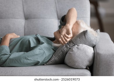 Older woman lying on sofa cushion, feeling fatigued, unmotivated, taking rest at home. Peaceful aged female having midday break, daytime nap indoors, relieving stress and mental or physical exhaustion - Powered by Shutterstock