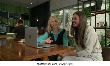 Older Woman Mentoring Younger Staff In Front Of Laptop Computer Inside Coffee Shop