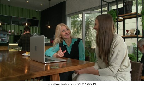 Older Woman Mentoring Younger Staff In Front Of Laptop Computer Inside Coffee Shop