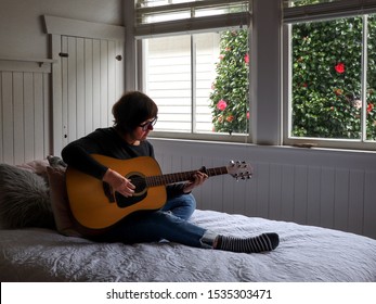 Older Woman Plays Her Guitar Indoors On Her Bed