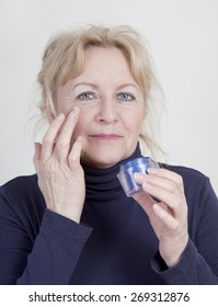 An Older Woman Is Putting Lotion On Her Eyes With A Wrinkle Cream