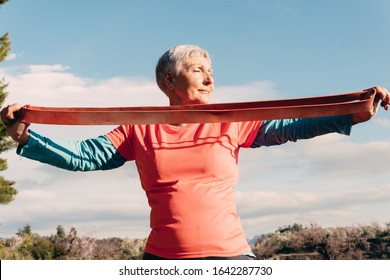 Older Woman With Red T Shirt And Elastic Band Practicing Sport In The Field