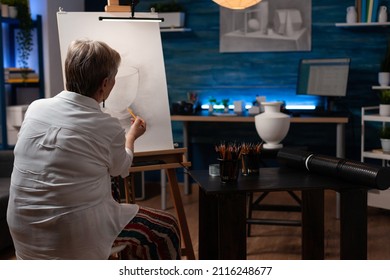 Older woman shading sketch in light study in evening class feeling inspired drawing still life vase model on paper canvas on easel. Focused retired art teacher doing creative artwork in pencil. - Powered by Shutterstock