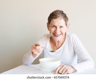 Older woman with short hair and white top laughing and eating soup from a white bowl - Powered by Shutterstock