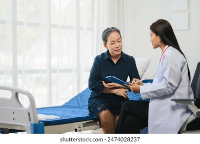 Older woman is sitting on a hospital bed with a doctor. The doctor is holding a clipboard and the woman doctor is looking at it. Scene is serious and focused - Powered by Shutterstock