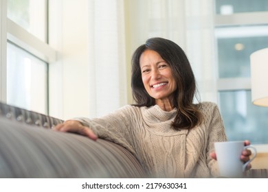 Older woman sitting on the sofa drinking coffee. - Shutterstock ID 2179630341