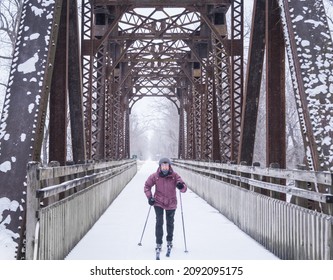 Older Woman Skiing Cross-country Under Old Railroad Bridge Transferred To State Recreation Trail On Snowy Winter Day In Midwest