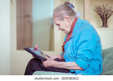 An Older Woman Is Talking Through A Tablet, A Modern Grandmother, A Silver Surfer, Sitting At Home, Retirees Stayed At Home Safe During Quarantine, Online Communication On The Internet.
