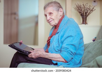 An Older Woman Is Talking Through A Tablet, A Modern Grandmother, A Silver Surfer, Sitting At Home, Retirees Stayed At Home Safe During Quarantine, Online Communication On The Internet.
