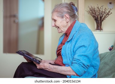 An Older Woman Is Talking Through A Tablet, A Modern Grandmother, A Silver Surfer, Sitting At Home, Retirees Stayed At Home Safe During Quarantine, Online Communication On The Internet.
