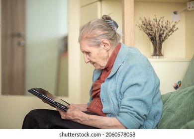 An Older Woman Is Talking Through A Tablet, A Modern Grandmother, A Silver Surfer, Sitting At Home, Retirees Stayed At Home Safe During Quarantine, Online Communication On The Internet.
