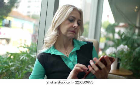 Older Woman Using Phone At Coffee Shop. Senior Businesswoman Typing Message On Smartphone At Cafe Place. Female Executive Looking At Cellphone