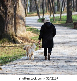 Older Woman Walking In Park With Her Dog