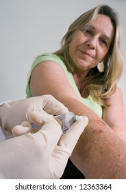 Older Woman Watching As A Doctor Is About To Apply Some Ointment To Her Arm