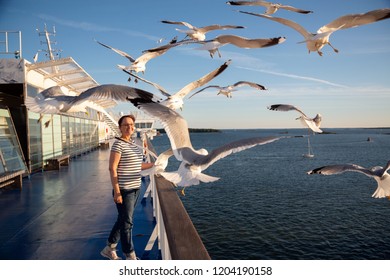 Older Woman Watching Seagulls Flying. Photo Of A Middle Aged Lady On The Cruise Ship Deck In A Baltic Sea Cruise.