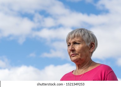 older woman with white hair and pink shirt with serious expression, blue sky background - Shutterstock ID 1521349253