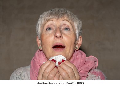 Older Woman With White Hair And Pink Scarf On Her Neck Sneezing