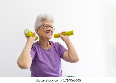 Older Woman With White Hair And Purple T-shirt Sportswear And Dark Tights Lifting Weights At Home
