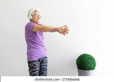 Older Woman With White Hair And Purple T-shirt Sportswear And Dark Tights Stretching At Home To Do Sport