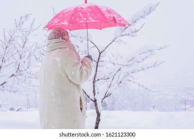 Older Woman With White Jacket And Red Umbrella Back With Snowy Background