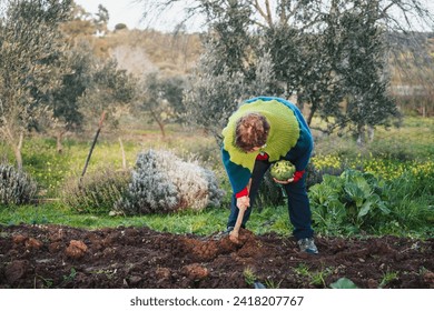 older woman working the garden soil with a harvested broccoli in her hand