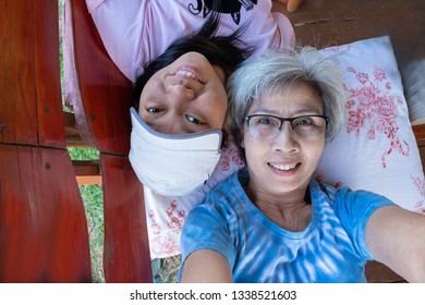 Older Woman And Younger Woman Lying Down On A Bench, Smiling And Looking At The Camera.