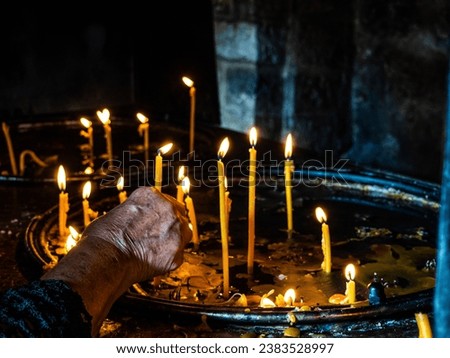 older woman's hand lighting a candle in church