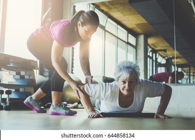 Older Women Doing Pushups. Young Personal Trainer Helping Senior Woman. Workout In Rehabilitation Center.